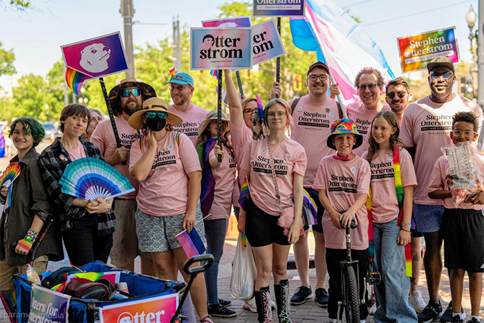 Group of people wearing pink shirts and holding rainbow flags and signs with drawings of otters