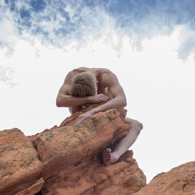 A photograph of a nude man wrapped around a stone resembling one of Goblin Valley's mushroom formations