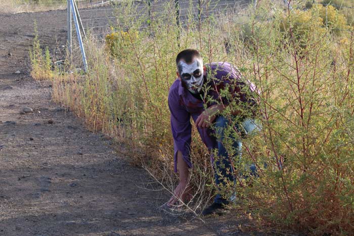 A man with zombie makeup crouches in a bush